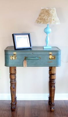 a blue suitcase sitting on top of a wooden table next to a lamp and framed photograph