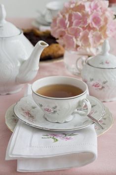 there is a tea cup and saucer on the table with pink flowers in the background