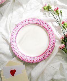 a pink and white plate sitting on top of a bed next to some red flowers