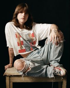 a woman sitting on top of a wooden table wearing ripped jeans and a white t - shirt