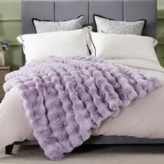 a bed with a purple blanket on top of it next to pillows and a night stand