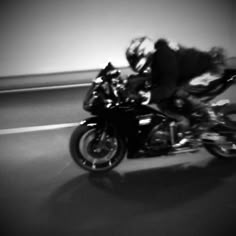 a man riding on the back of a motorcycle down a street next to a wall