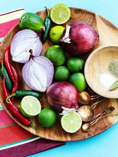 a wooden plate topped with onions, limes and other vegetables on top of a table