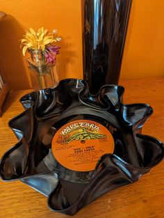 a black vase with flowers in it on a wooden table next to a record player