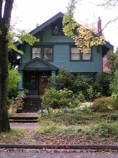 a green house with stairs leading up to it's front door and trees in the foreground