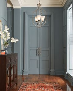 a hallway with blue walls and wooden floors, an ornate chandelier hangs from the ceiling