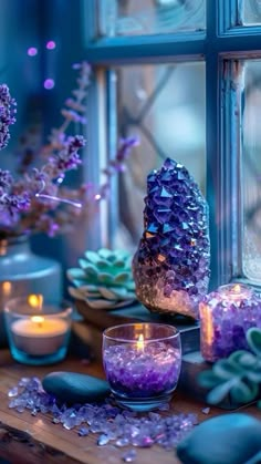 a table with candles, rocks and flowers in front of a glass window sill