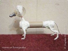 a dog made out of toilet paper on top of a red rug with a light bulb in it's mouth