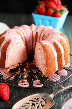 a bundt cake with pink icing on a cooling rack next to strawberries