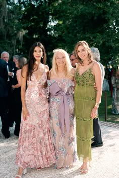 three women standing next to each other at a formal event with people in the background