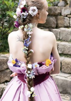 a woman in a dress with flowers on her head is standing near a stone wall