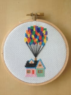 a cross stitch picture with a house and a hot air balloon in the shape of a house