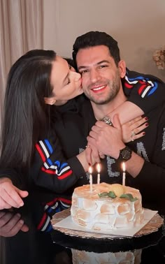 a man and woman are kissing in front of a cake with candles on it while sitting next to each other