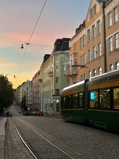 a green train is going down the tracks in front of some buildings and cars at sunset