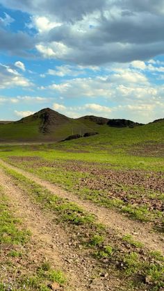 a dirt road in the middle of an open field with green grass and hills behind it