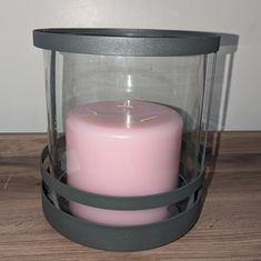 a pink candle sitting inside of a glass container on a wooden table next to a wall