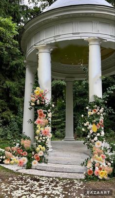 an outdoor gazebo with flowers and greenery around it