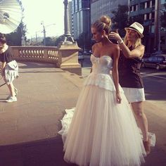 two women in dresses and hats are standing on the sidewalk while another woman takes a photo