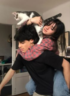 a man is holding a cat on his shoulders in the living room while another woman holds him