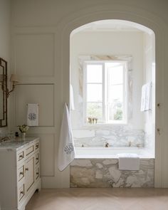 a white bathroom with an arched window and stone bathtub