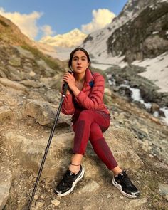 a woman sitting on top of a rock next to a snow covered mountain side holding a ski pole