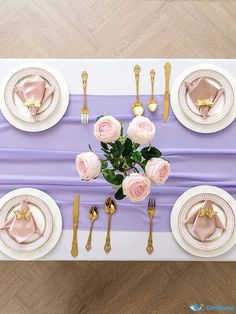 the table is set with pink roses and gold place settings