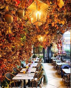 an outdoor dining area with tables and chairs covered in autumn leaves, hanging from the ceiling