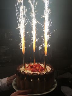 a cake with strawberries and sparklers on top is being held by two hands