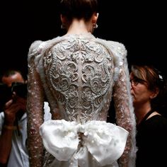 the back of a woman's white wedding dress with an intricate lace and bow