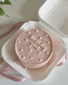 a pink birthday cake with white hearts on it in a plastic container next to a flower