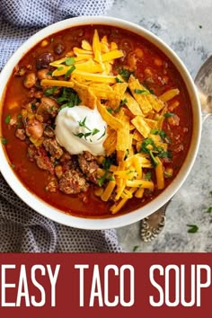 a white bowl filled with chili and cheese on top of a blue towel next to a spoon