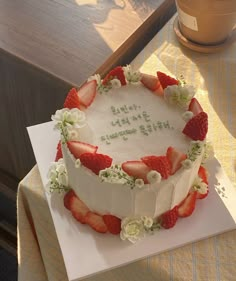 a white cake with strawberries and flowers on it sitting on top of a table