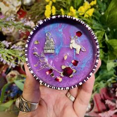 a person holding up a purple plate with flowers in the background and a unicorn on it