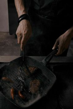 a man cooking food on top of a grill with tongs and a spatula