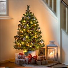 a small christmas tree with lights and presents on the floor in front of a staircase