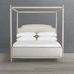 a bed with white linens and pillows on top of it, in front of a gray wall