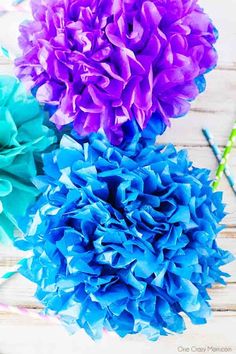 three blue and purple flowers sitting on top of a white wooden table next to scissors