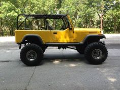 a yellow jeep is parked on the side of the road in front of some trees