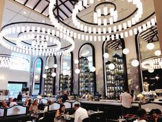 people sitting at tables in a restaurant with chandeliers hanging from the ceiling and windows