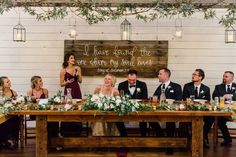 a group of people sitting at a table with flowers and greenery in front of them