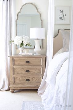 a bedroom with a bed, mirror and flowers on the dresser in front of it