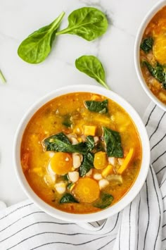 two bowls of soup with spinach leaves on the side