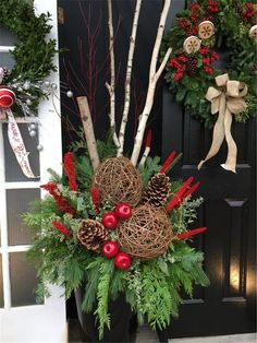 a planter filled with christmas wreaths and pine cones in front of a door