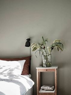 a bedroom with a bed, nightstand and plants in a vase on the end table