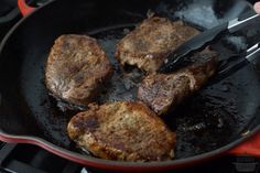 steaks being cooked in a skillet on top of the stove with tongs