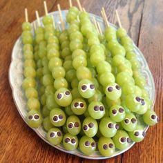 green grapes with googly eyes are arranged on a white plate and toothpicks sticking out of them