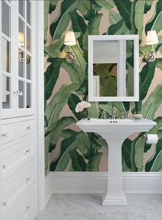 a white pedestal sink sitting under a mirror next to a green leaf wallpapered bathroom