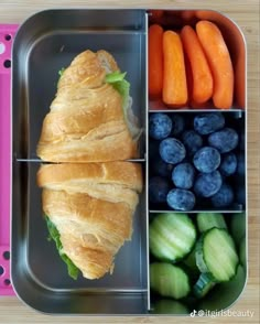 a bento box filled with fruits and vegetables next to a croissant sandwich