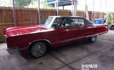 an old red car parked in a driveway next to a wooden fence and some trees