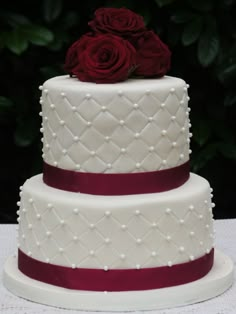 a three tiered wedding cake with red roses on top